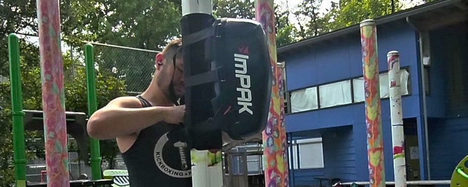 Man setting up ImPAK bag on a pole in a playground with colorful poles and a building in the background
